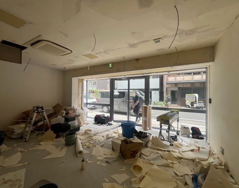 施工前：壁と天井のクロスを剥がし、床一面に剥がした壁紙が広がった道路沿いの主室